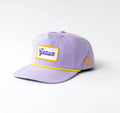 A light purple baseball cap with a yellow embroidered border around a white front patch reading 'Gaul' in blue script, and a small yellow circular patch on the side, photographed on a light gray background.