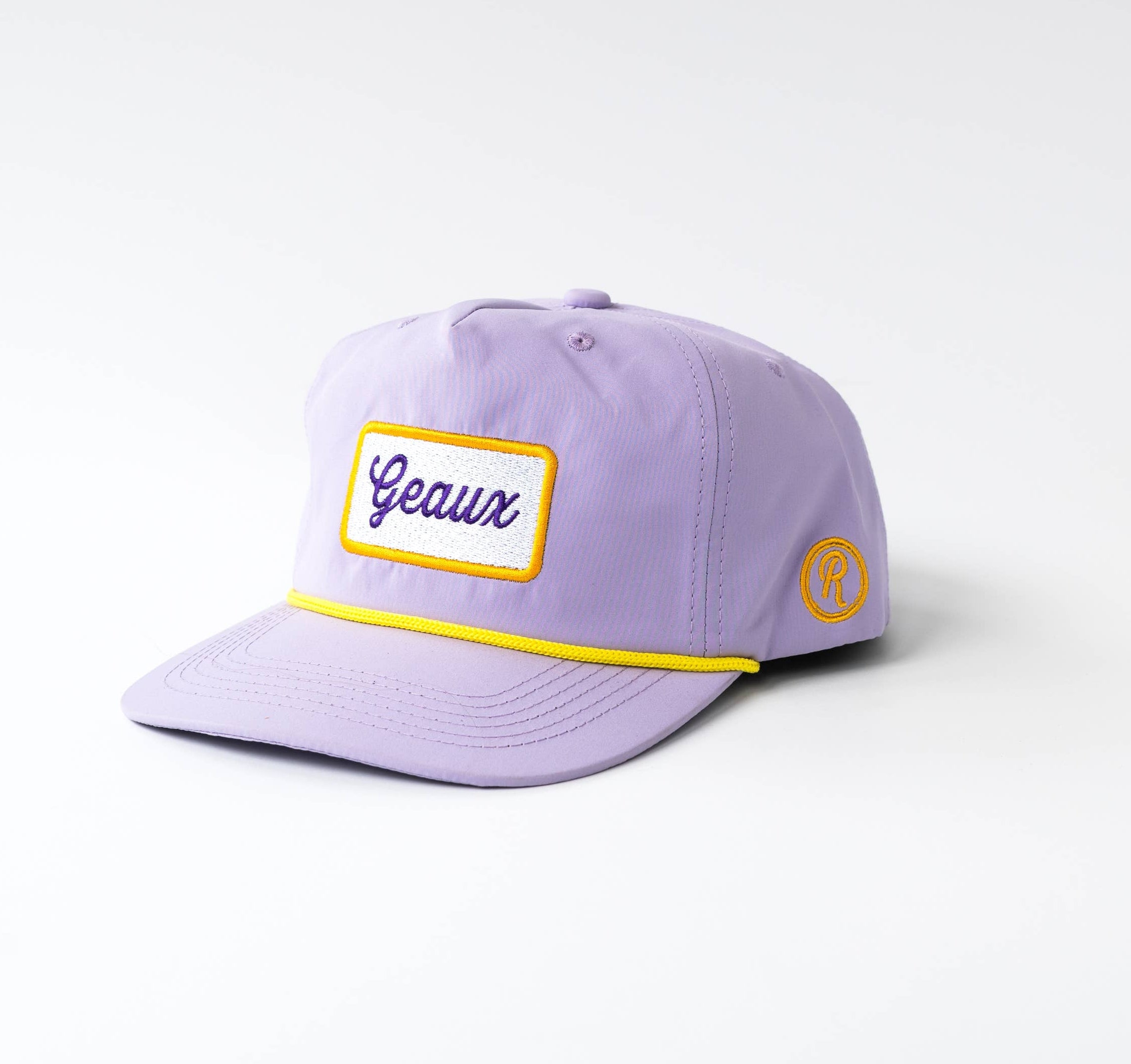 A light purple baseball cap with a yellow embroidered border around a white front patch reading 'Gaul' in blue script, and a small yellow circular patch on the side, photographed on a light gray background.